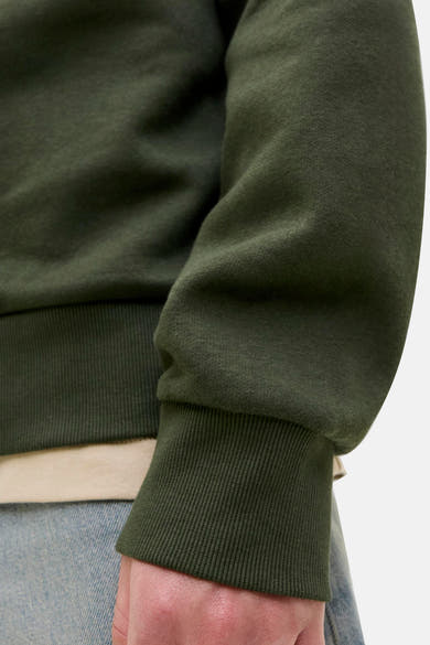 Groene sweater van Originals by Jack & Jones, met geribde boorden, gedragen met een beige T-shirt en een blauwe jeans.