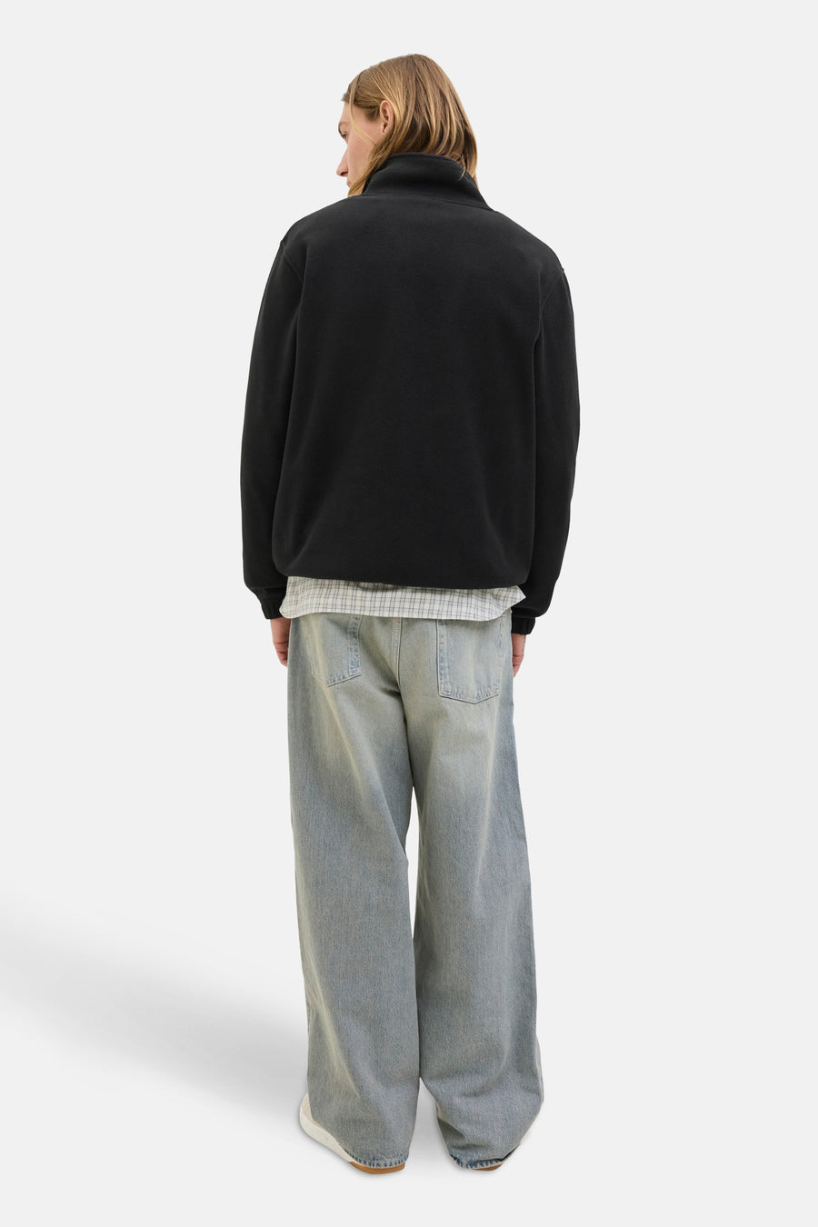 Polaire noire de JACK & JONES, avec col montant, portée avec une chemise à carreaux et un jean ample.