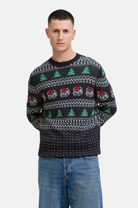 Pull à col rond bleu de JACK & JONES, avec motifs de sapins de Noël et cadeaux, porté avec un jean.
