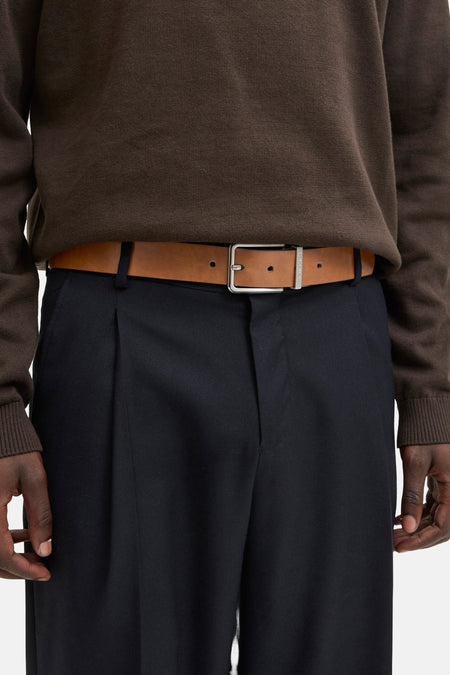 Bruine leren riem, van ACCESSORIES BY JACK & JONES, gedragen met een marineblauwe pantalon en een bruine trui.