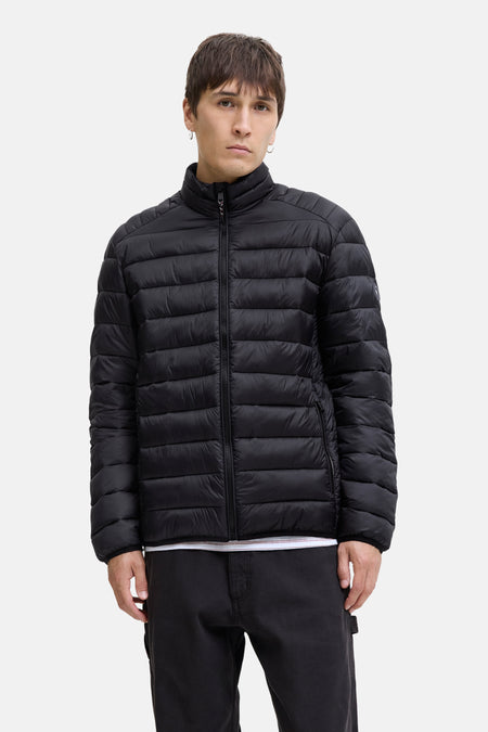 Veste de pluie noire par JACK & JONES, matelassée avec fermeture éclair et poches zippées, portée avec un pantalon noir.