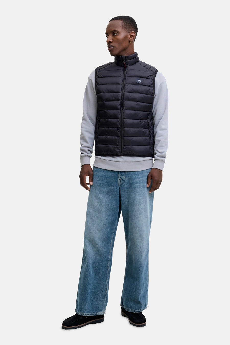 Veste sans manches noire de JACK & JONES, portée sur un pull gris et un jean ample bleu.