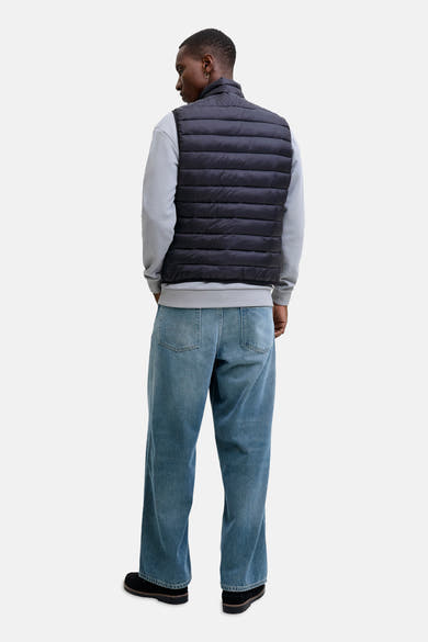 Veste sans manches noire de JACK & JONES, portée sur un sweat gris avec un jean bleu ample.