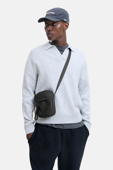 Zwarte schoudertas van ACCESSORIES BY JACK & JONES met schouderriem, gedragen door een man met een grijze trui en pet.