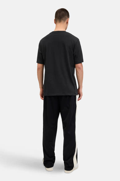Zwart T-shirt met korte mouwen van JACK & JONES, gedragen met een zwarte joggingbroek met witte strepen.