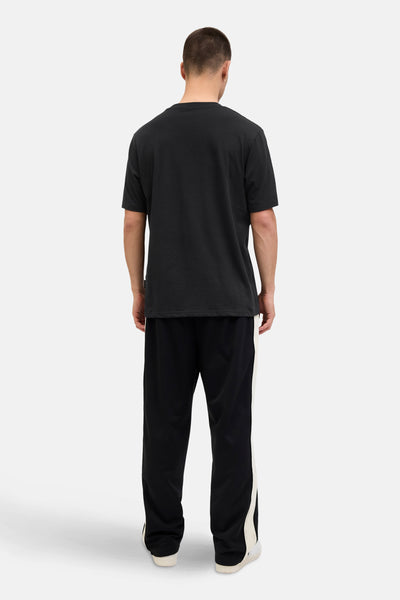 T-shirt noir à manches courtes de JACK & JONES, porté avec un pantalon de survêtement noir à rayures blanches.