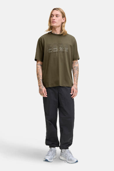 Groen T-shirt met korte mouwen van JACK & JONES, met 'Core'-opdruk op de voorkant, gedragen met een zwarte joggingbroek.