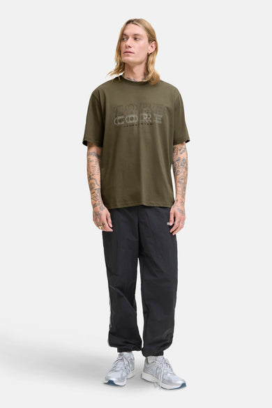 Groen T-shirt met korte mouwen van JACK & JONES, met 'Core'-opdruk op de voorkant, gedragen met een zwarte joggingbroek.