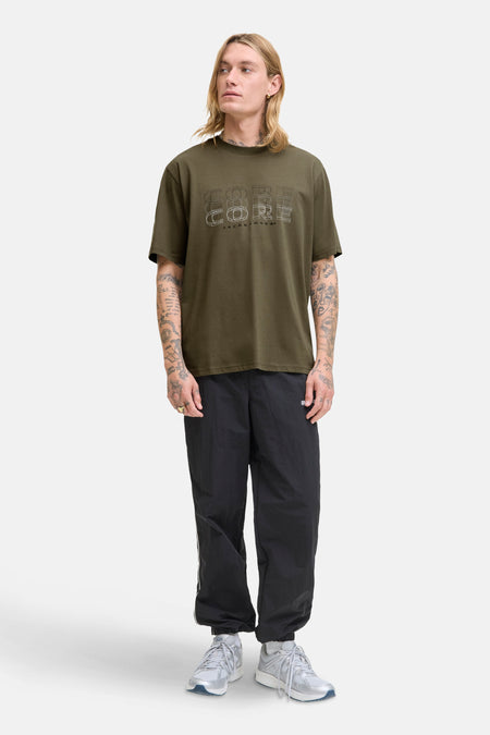 Groen T-shirt met korte mouwen van JACK & JONES, met 'Core'-opdruk op de voorkant, gedragen met een zwarte joggingbroek.
