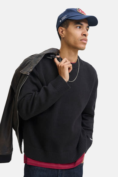 Zwarte rondehals trui van ORIGINALS BY JACK & JONES met een gebreid patroon, gedragen met een pet en een jas.