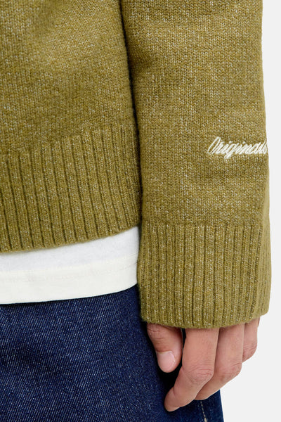Pull à col rond vert d'ORIGINALS BY JACK & JONES, avec une broderie décorative sur la manche et un jean bleu foncé visible.