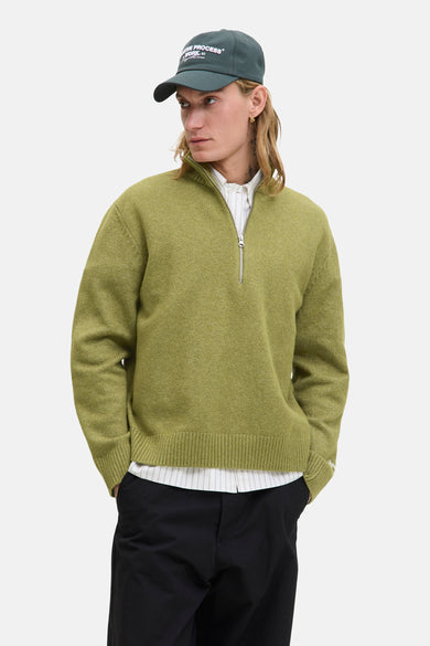 Groene trui met ronde hals van ORIGINALS BY JACK & JONES, gedragen met een gestreept overhemd en een pet.