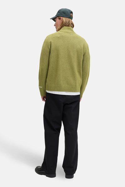 Groene rondehals trui van ORIGINALS BY JACK & JONES, gedragen met een wijde zwarte broek en een groene pet.