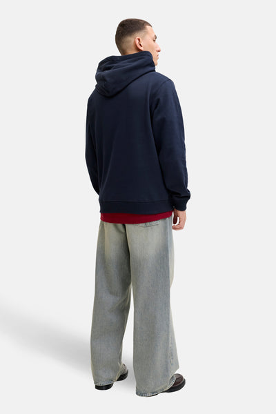 Blauwe hoodie van PREMIUM by JACK & JONES, gedragen met een rood T-shirt en een grijze wijde jeans.
