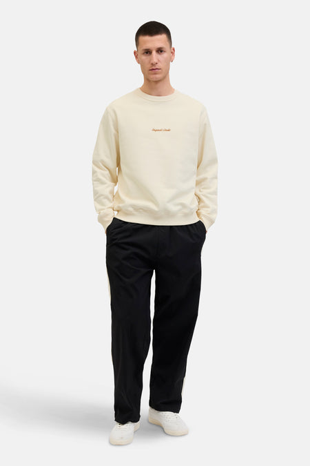 Ecru ronde hals sweatshirt van ORIGINALS BY JACK & JONES, gedragen met een zwarte broek met witte bies en witte sneakers.