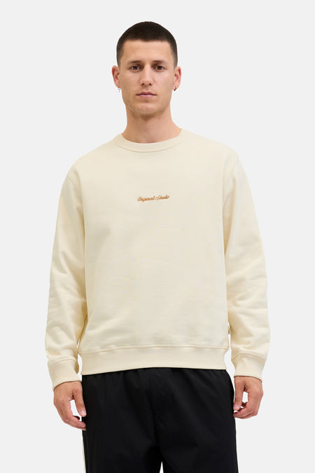 Ecru ronde hals sweatshirt van ORIGINALS BY JACK & JONES, met geborduurd logo, gedragen met een zwarte broek.