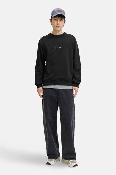 Zwarte rondehals sweatshirt van ORIGINALS BY JACK & JONES, gedragen met een grijs T-shirt, een wijde zwarte jeans en sneakers.