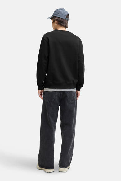 Zwarte rondehals sweatshirt van ORIGINALS BY JACK & JONES, gedragen met een wijde zwarte jeans en een lichtblauwe pet.