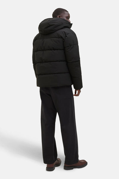 Zwarte regenjas van ORIGINALS BY JACK & JONES, met capuchon, gedragen met een bruine broek en schoenen.