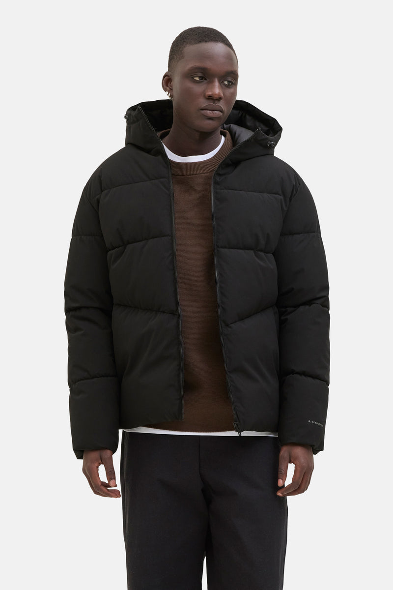Zwarte regenjas van ORIGINALS BY JACK & JONES, met capuchon, gedragen over een bruine trui en een wit T-shirt.