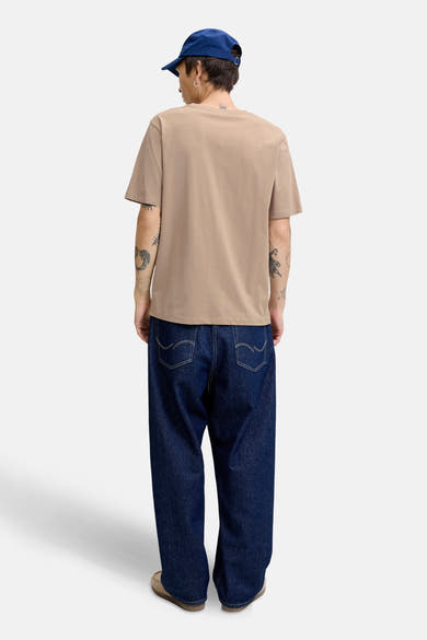 Beige T-shirt met korte mouwen van ORIGINALS BY JACK & JONES, gedragen met een wijde jeans en een blauwe pet.