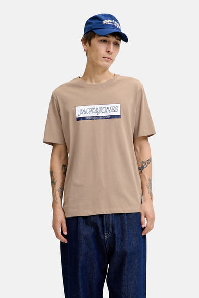 Beige T-shirt met korte mouwen van ORIGINALS BY JACK & JONES, met logo op de voorkant, gedragen met een blauwe hoed en een spijkerbroek.