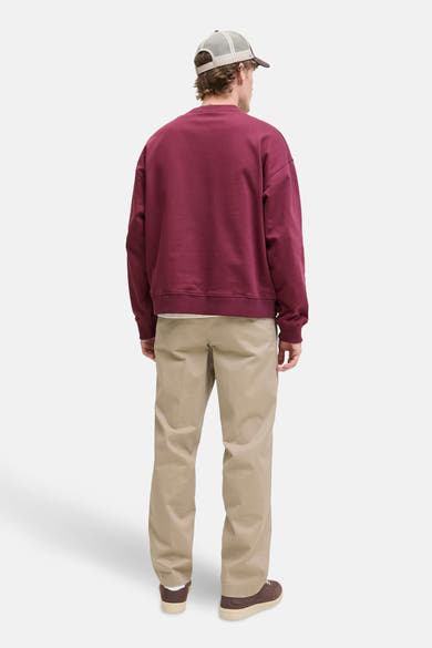 Beige chino broek van JACK & JONES JEANS INTELLIGENCE, gedragen met een bordeauxrode sweater en een pet.