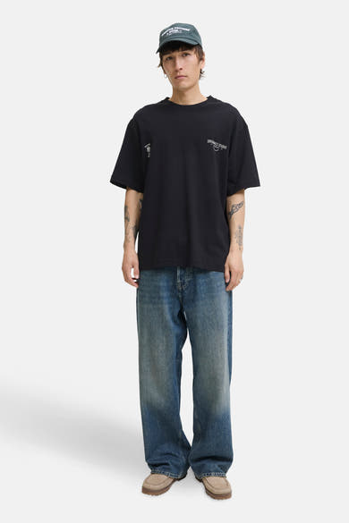 Zwart T-shirt met korte mouwen van PREMIUM by JACK & JONES, gedragen met een wijde blauwe jeans en een groene pet.