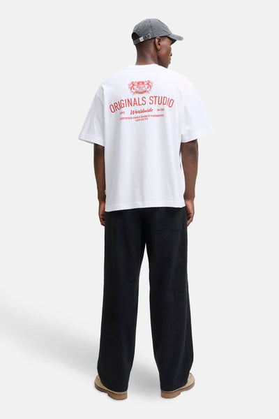 Wit T-shirt met korte mouwen van PREMIUM by JACK & JONES, met rode print op de rug, gedragen met een wijde zwarte broek en een pet.