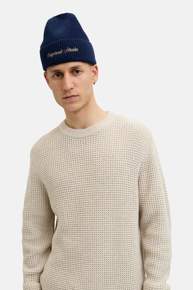 Bonnet bleu marine de ACCESSORIES BY JACK & JONES, avec inscription dorée, porté avec un pull en maille beige.