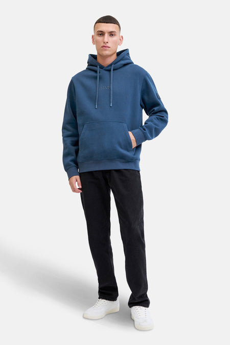 Blauwe hoodie van JACK & JONES, gedragen met een zwarte broek en witte sneakers.