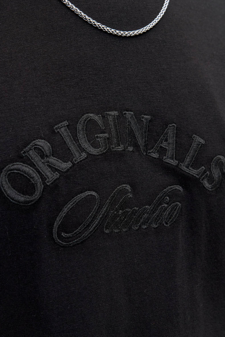 Zwart T-shirt met korte mouwen van JACK & JONES met geborduurde "Originals Studio" letters en zilveren ketting.