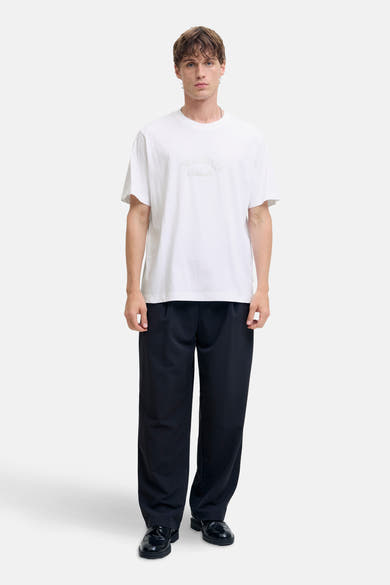 T-shirt blanc à manches courtes de JACK & JONES, porté avec un pantalon noir ample et des chaussures vernies noires.