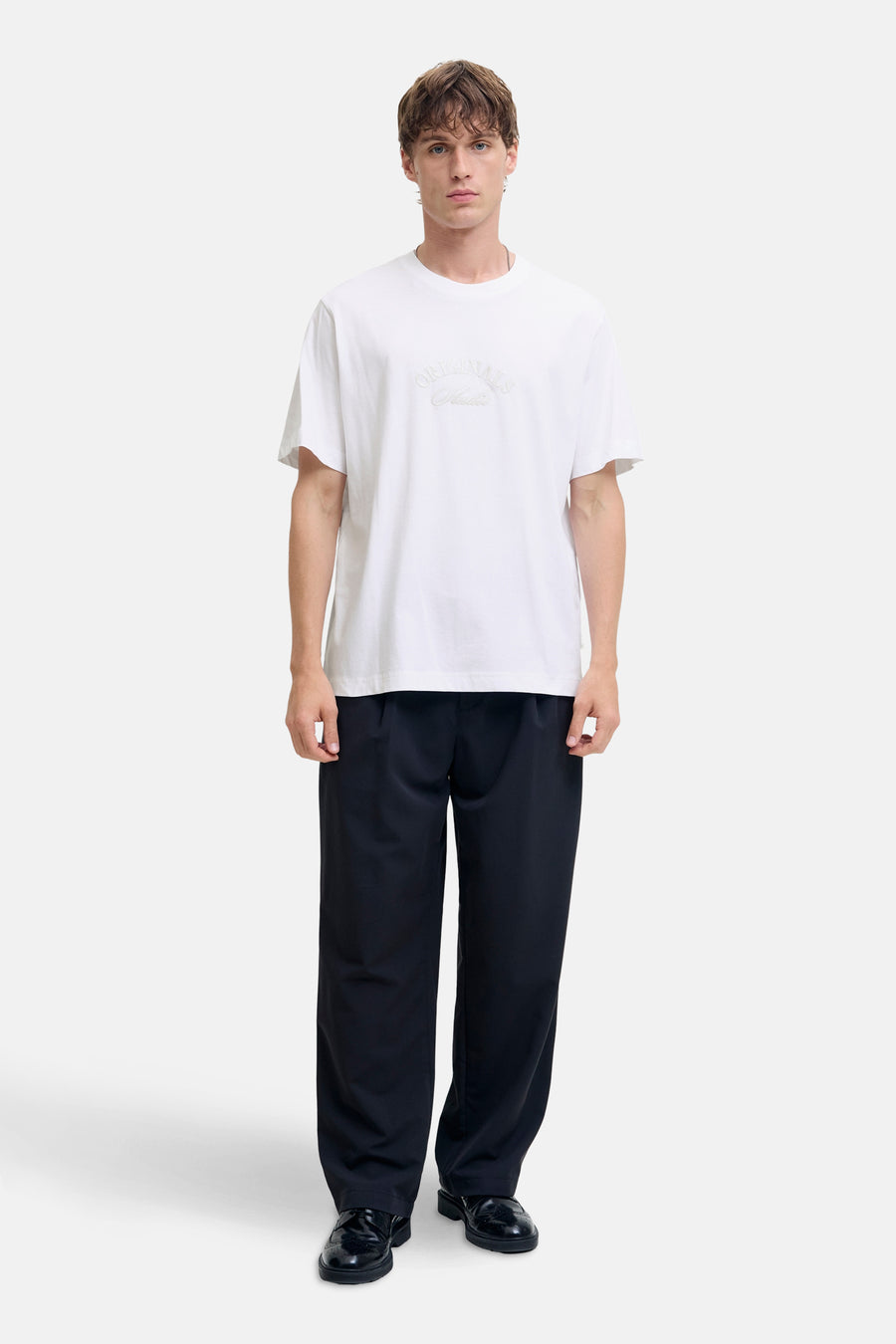 T-shirt blanc à manches courtes de JACK & JONES, porté avec un pantalon noir ample et des chaussures vernies noires.