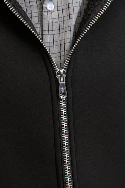 Gilet noir de JACK & JONES avec fermeture éclair argentée, sur une chemise à carreaux gris.
