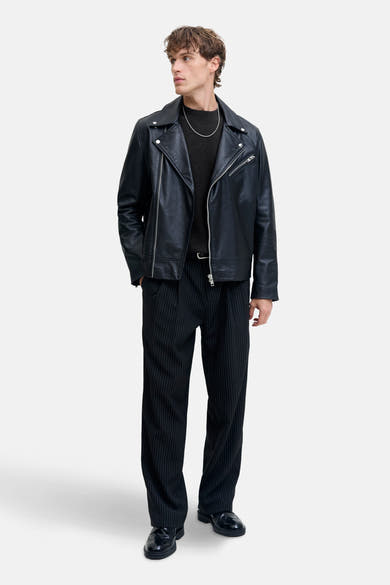 Zwart poloshirt met korte mouwen van JACK & JONES, gedragen met een leren jack en een gestreepte broek.