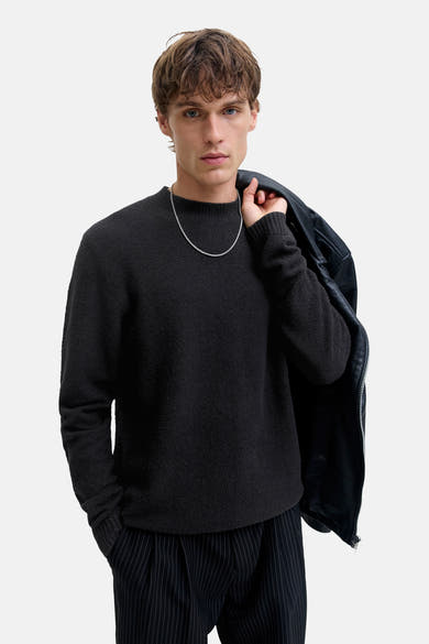 Zwart poloshirt met korte mouwen van JACK & JONES, gedragen met een gestreepte broek en een zilveren ketting.