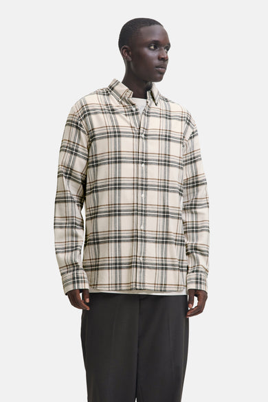 Chemise à manches longues beige de JACK & JONES, à carreaux marron et noirs, portée avec un t-shirt blanc et un pantalon foncé.