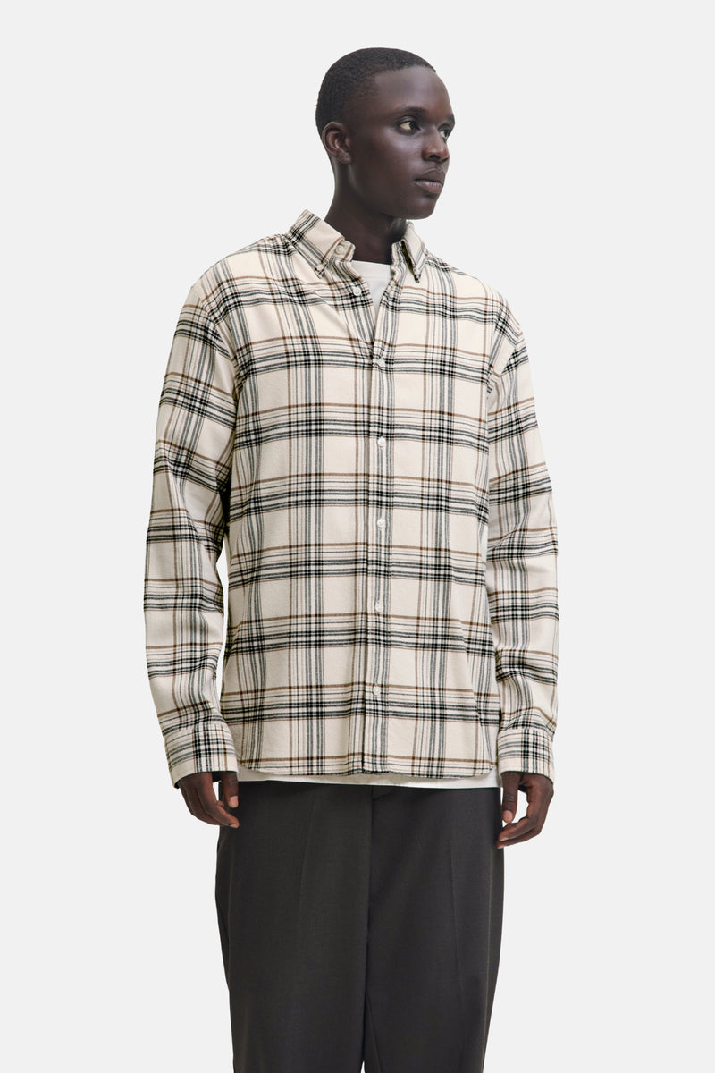 Chemise à manches longues beige de JACK & JONES, à carreaux marron et noirs, portée avec un t-shirt blanc et un pantalon foncé.