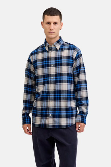 Chemise à manches longues bleue à carreaux, par JACK & JONES, portée avec un pantalon bleu marine.