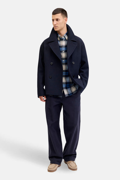 Chemise à manches longues bleue de JACK & JONES avec motif à carreaux porté avec un caban et un pantalon bleu marine.
