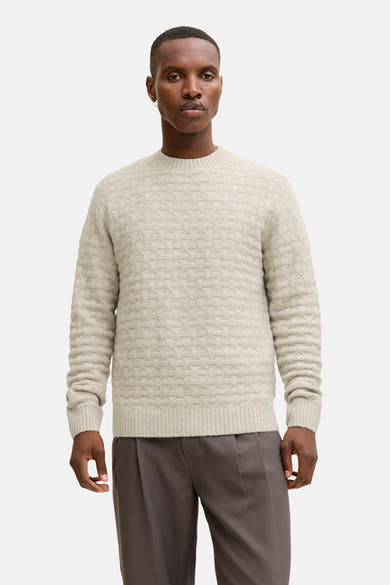 Ronde hals trui met kabelsteek van JACK & JONES, gedragen met een camelkleurige jas en een grijze broek.