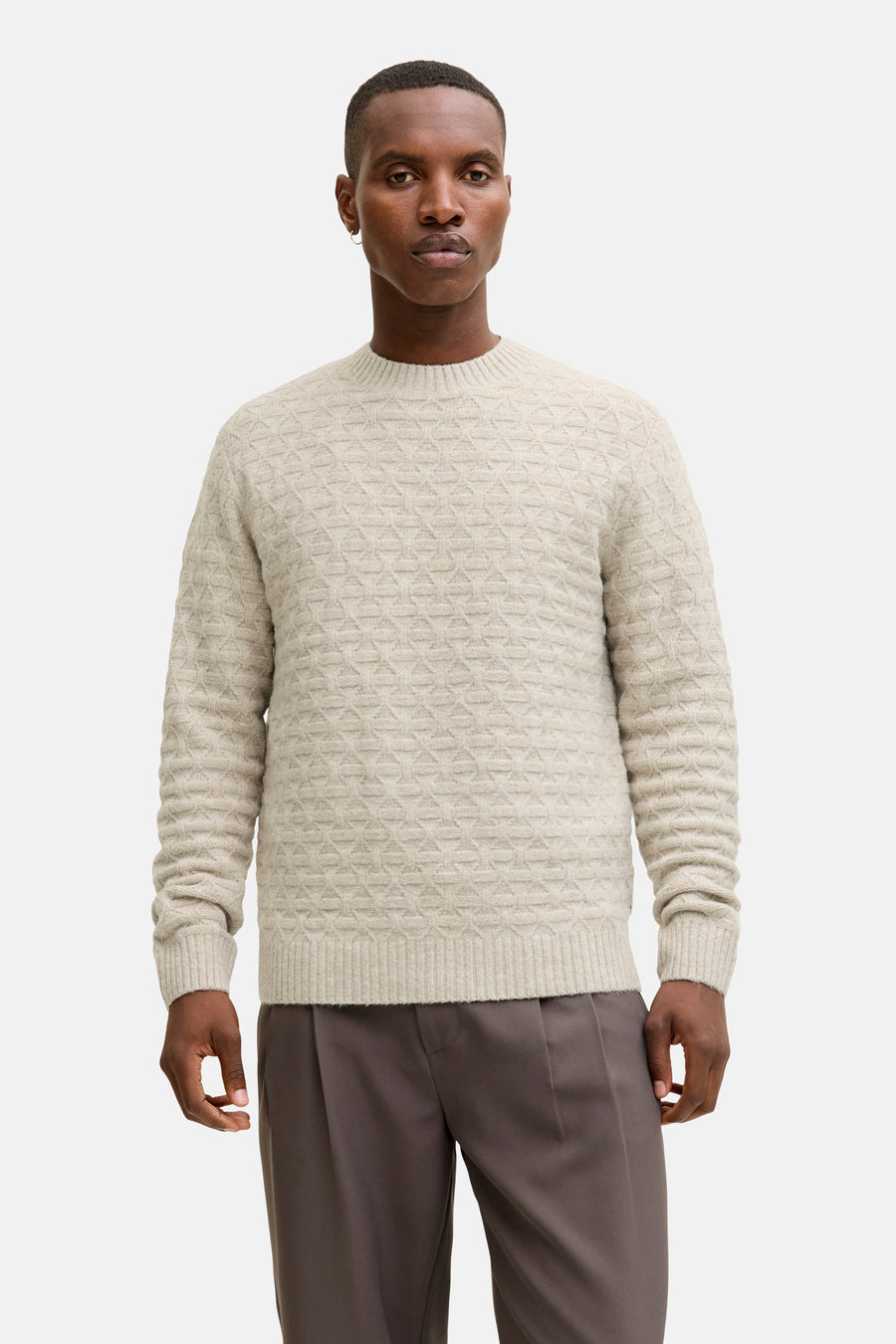 Ronde hals trui met kabelsteek van JACK & JONES, gedragen met een camelkleurige jas en een grijze broek.