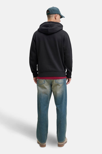 Zwarte hoodie van JACK & JONES, gedragen met een lichtgewassen spijkerbroek en een donkergroene pet.