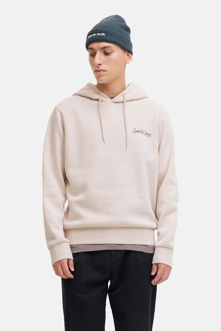 Beige hoodie van JACK & JONES, gedragen met een donkergroene muts, een zwarte broek en beige schoenen.