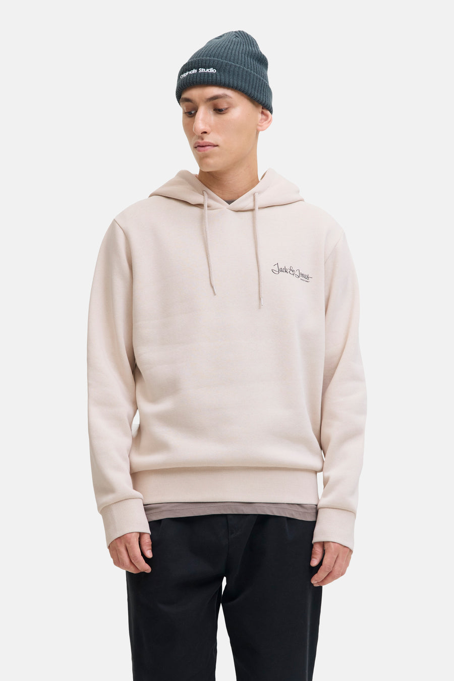 Beige hoodie van JACK & JONES, gedragen met een donkergroene muts, een zwarte broek en beige schoenen.