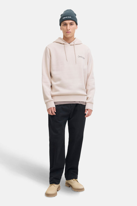 Sweat à capuche beige de JACK & JONES, porté avec un bonnet vert foncé, un pantalon noir et des chaussures beiges.