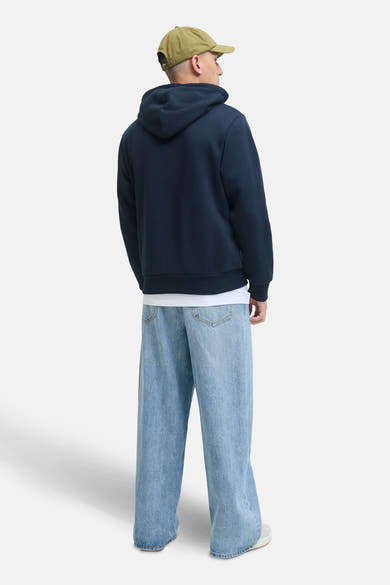 Blauwe hoodie van JACK & JONES gedragen met een wijde spijkerbroek en een olijfgroene pet, achteraan gezien.