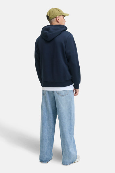 Blauwe hoodie van JACK & JONES gedragen met een wijde spijkerbroek en een olijfgroene pet, achteraan gezien.