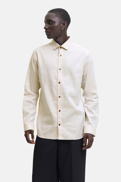 Chemise beige à manches longues de PREMIUM by JACK & JONES, avec boutons marron et portées avec un pantalon noir.